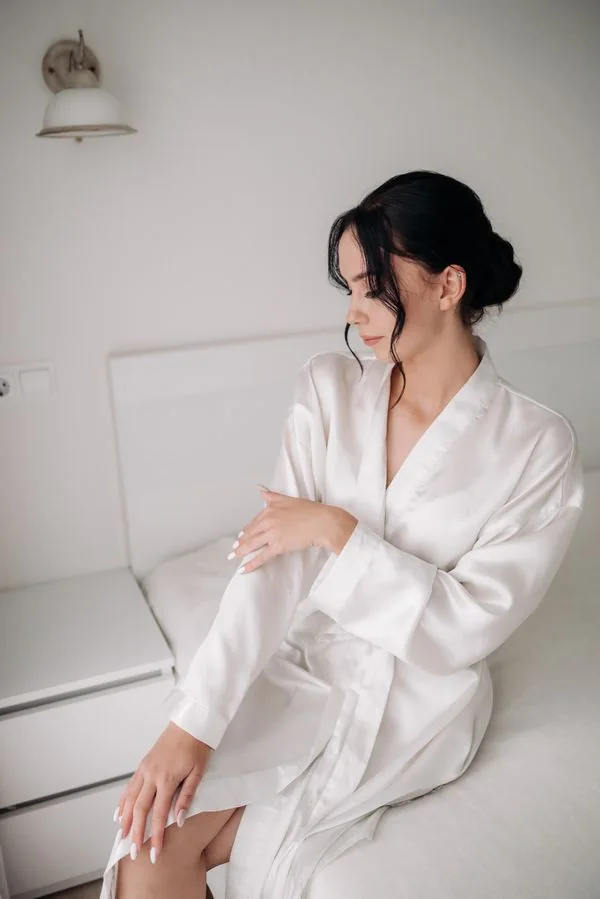 Ivory satin nightgown with adjustable straps draped on a bed